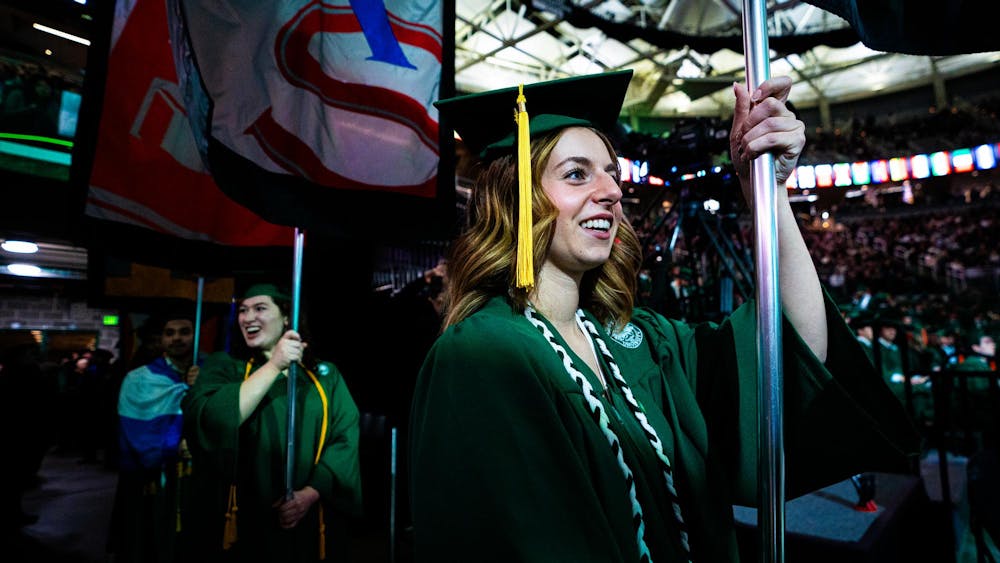 MSU alumni march onto the floor with their college flags during the fall 2024 commencement ceremony at the Breslin Center on Dec. 14, 2024.