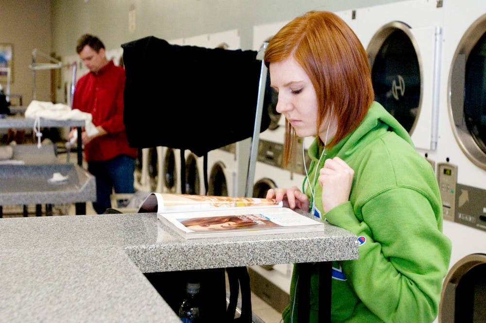 Clinical laboratory sciences senior Nicole Brereton reads a magazine as she waits for her clothes to dry Tuesday at Point Laundry, 2800 E. Grand River Ave. Many students have been choosing to wash their clothes at a laundromat or other services, rather than the dorms. Derek Berggren/The State News