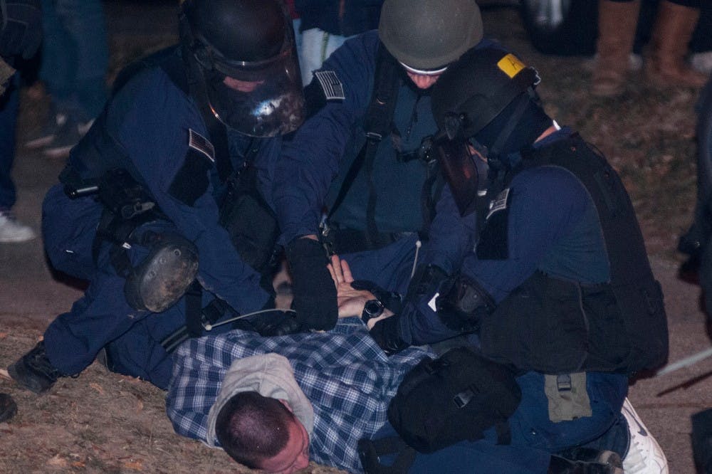 <p>Police outfitted in riot gear take down a participant during a riot in the streets of Cedar Village on Dec. 8, 2013. The police and fire department responded to multiple riots and fires across East Lansing.</p>