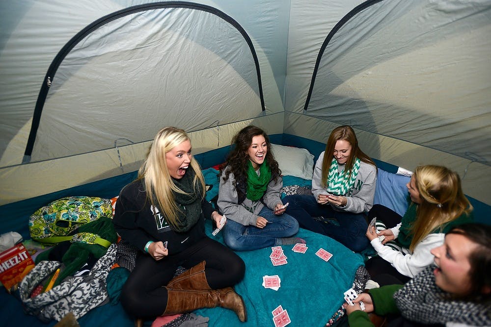 <p>From left, elementary education junior Anna Ralph, nutritional sciences junior Megan Altizer, mathematics sophomore Taylor Dewildt-Christensen, nutritional sciences sophomore Cecilia DeWys and mathematics senior Kelli Egeler play a card game in their tent Oct. 17, 2014, during the Izzone Campout at Munn Field. Hundreds of students battled the cold and rain to sleep outdoors overnight in hopes of getting lower bowl seating. Julia Nagy/The State News</p>