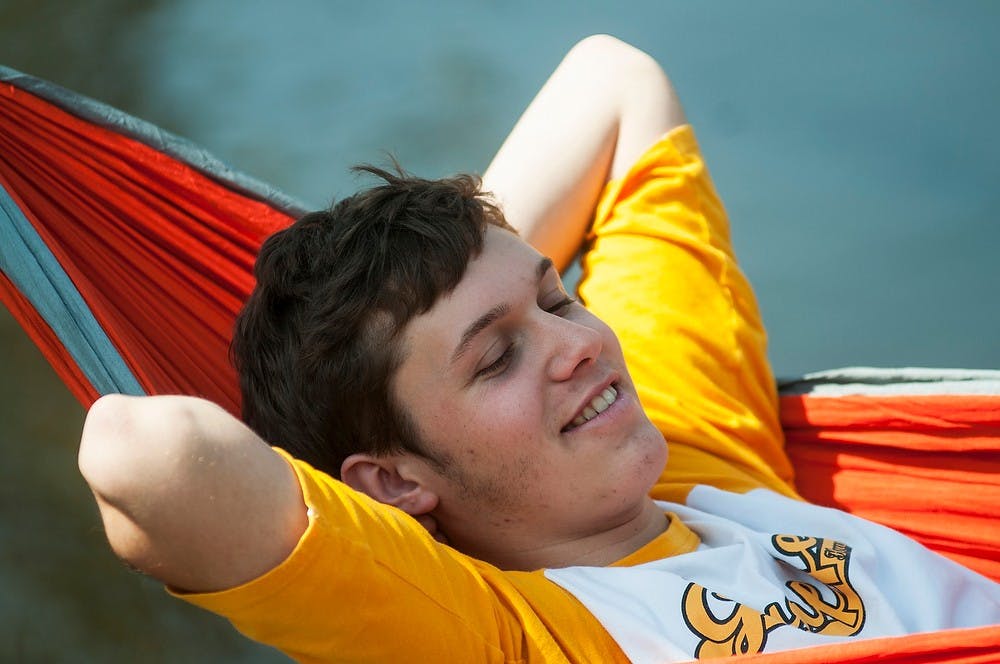 <p>Advertising sophomore Alex Byers sits in a hammock April 10, 2014, along the Red Cedar River behind the Administration Building. Byers, part of the Hammocking Club of MSU, had set up a hammock with a fellow club member. Danyelle Morrow/The State News</p>