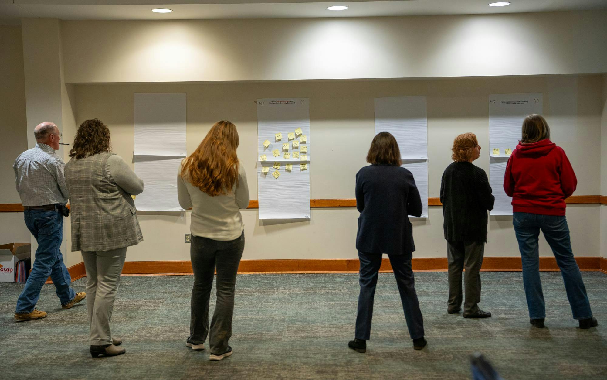 Community members write down their answers on a sticky note answering a question on a big sheet of paper on the wall during an activity of the MSU Extension’s East Lansing public listening session at the Hannah Community Center on Nov. 29, 2023. 