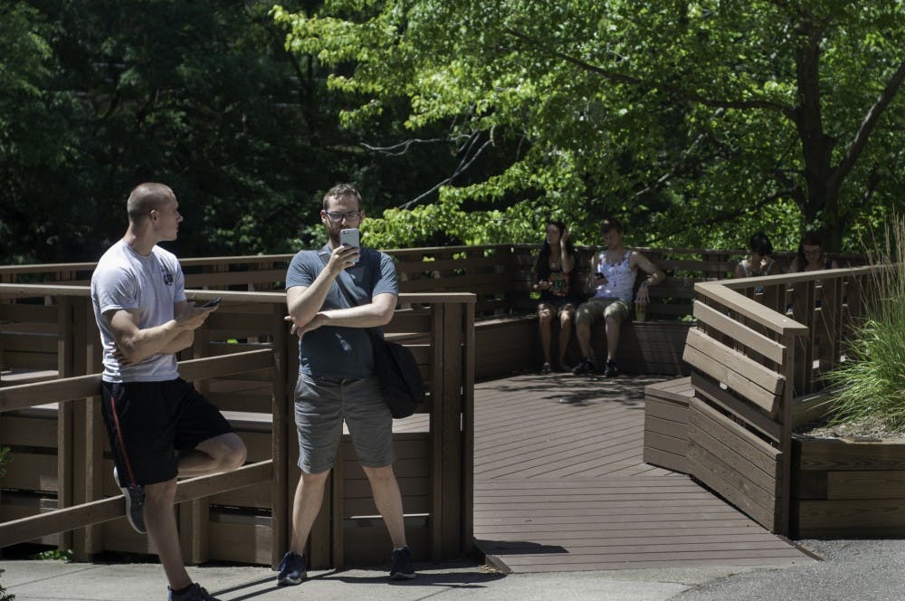 Supply chain senior Spencer Holland, left, and social work graduate student Patrick Zimmer play Pokemon Go on July 12, 2016 along the Red Cedar River. Zimmer said he had traveled 38.8 kilometers or 24.1 miles while playing the game.