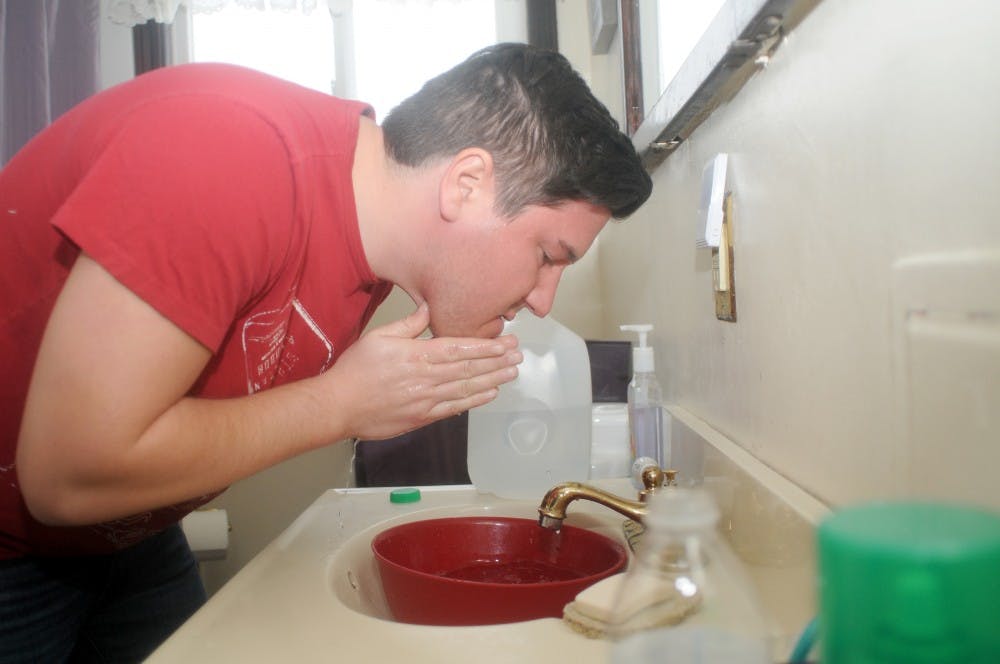 Interdisciplinary studies in social science senior Ricardo Vasquez demonstrates washing his face using water he poured from a bottle on Feb. 12, 2016 at his home in Flint, Mich. Vasquez relies on bottled water to complete daily tasks since it isn't safe to use the tap water in his home. 