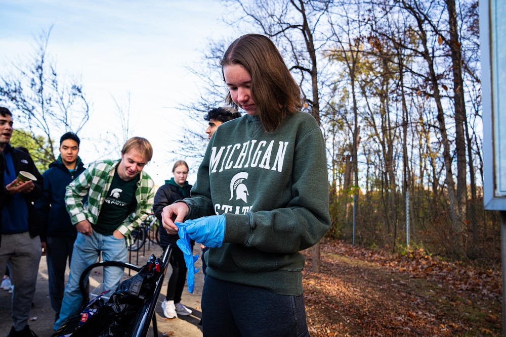 A student puts on a pair of nitrile gloves moments before an invasive species removal effort begins at the Baker Woodlot on Nov. 9, 2024.