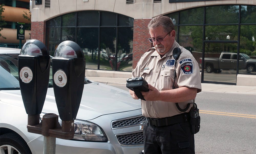 <p>P.A.C.E Officer Paul Weidner of East Lansing writes a ticket for an expired meter on Albert Avenue July 10, 2015. If the driver comes out to their car while he is writing the ticket, Weidner uses his discretion to decide whether to issue the ticket or issue a warning. Catherine Ferland/ The State News</p>