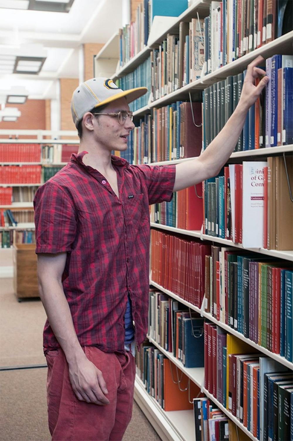 <p>Media and information junior Richie Jeczen organizes books on the book shelf May 22, 2015 while working in the Engineering Library. Jeczen studies here during his free time while working late shifts. Asha Johnson/The State News</p>