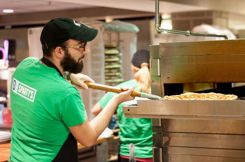 <p>International relations sophomore John Elias takes a pizza out of the oven Sept. 29, 2014, at Case Hall Sparty's. "I feel like it's a step in the right direction, but further progress needs to be made," Elias said. Dylan Vowell/The State News.</p>