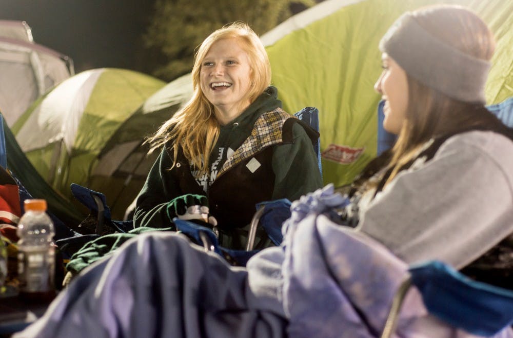 <p>Supply chain management senior Erika Roe, center, laughs while talking with child development junior Katie Immel on Oct. 9, 2015, during the Izzone Campout at Munn Field. This annual event consists of students staying throughout the night in hopes of getting lower bowl seating. </p>
