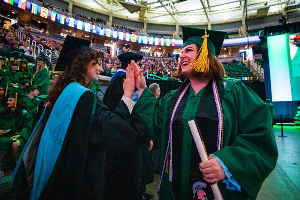 An MSU alumnus high fives a professor during the fall 2024 commencement ceremony at the Breslin Center on Dec. 14, 2024.