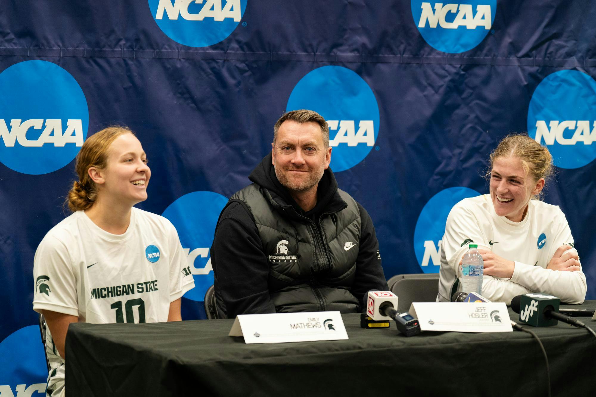 <p>Michigan State University women's soccer players graduate midfielder Emily Mathews (10) and graduate midfielder Justina Gaynor (18), along with head coach Jeff Hosler, talk to the press during a postgame press conference after the NCAA tournament game against Western Michigan University on Nov. 16, 2024. The Spartans defeated the Broncos, 3-1.</p>