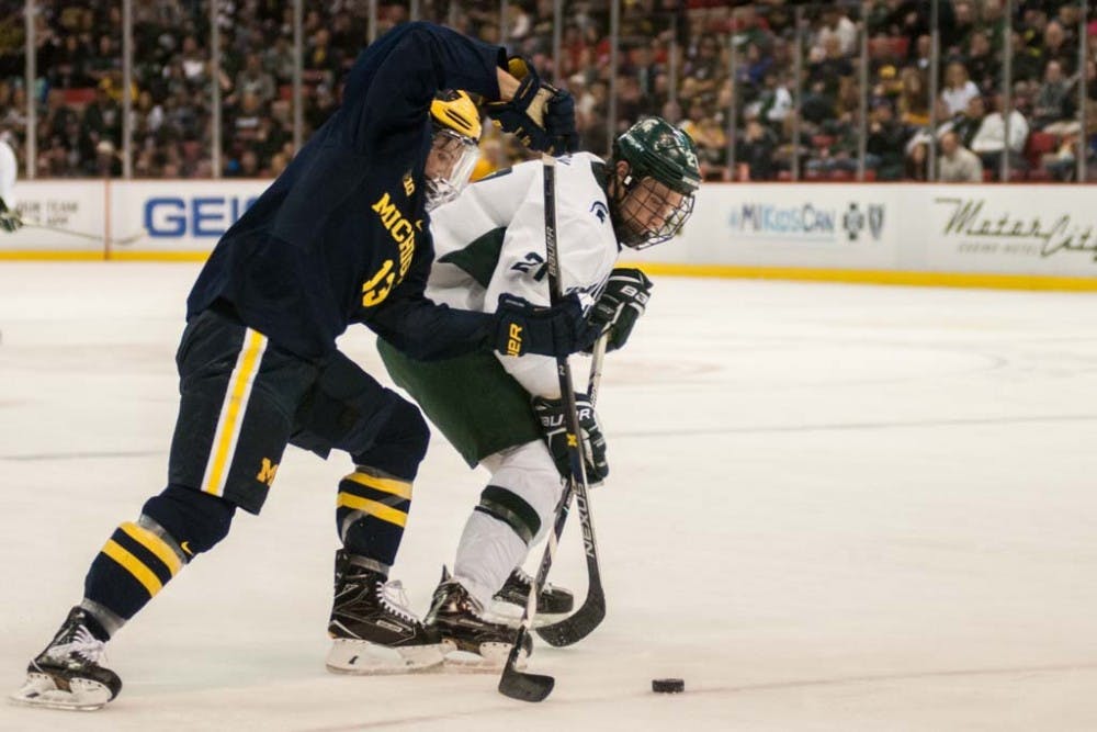 Senior forward Joe Cox (21) fights to maintain possession of the puck against Michigan forward Jake Slaker (13) during the first period of the men?s hockey game against the University of Michigan on Feb. 10, 2017 at Joe Louis Arena in Detroit. The Spartans were defeated by the Wolverines in an overtime shootout, 5-4. 