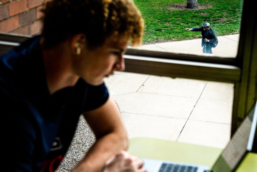 Michigan State University business freshman Logan Aguirre, 18, works inside Wells Hall while Pastor Michael Venyah preaches outside in People’s Park, seen through a window on Michigan State University’s campus in East Lansing, Mich., on Monday, April 13, 2026.