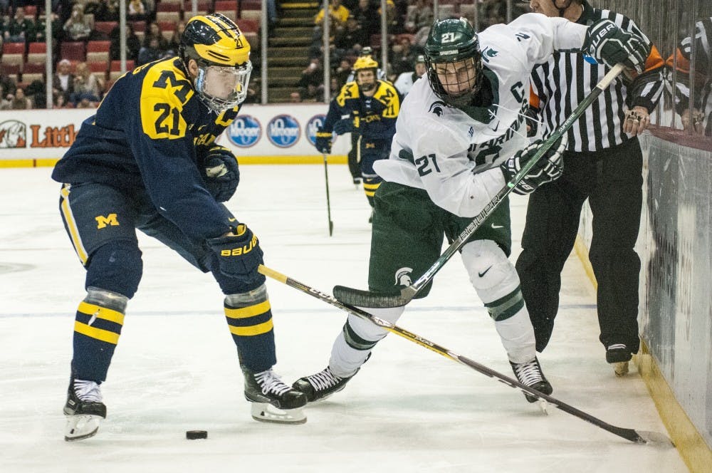 Senior wingman Joe Cox (21) and Michigan defenseman Nolan De Jong (21) fight for the puck during the third period of the 52nd Annual Great Lakes Invitational third-place game against the University of Michigan on Dec. 30, 2016 at Joe Louis Arena in Detroit. The Spartans were defeated by the Wolverines in overtime, 5-4.