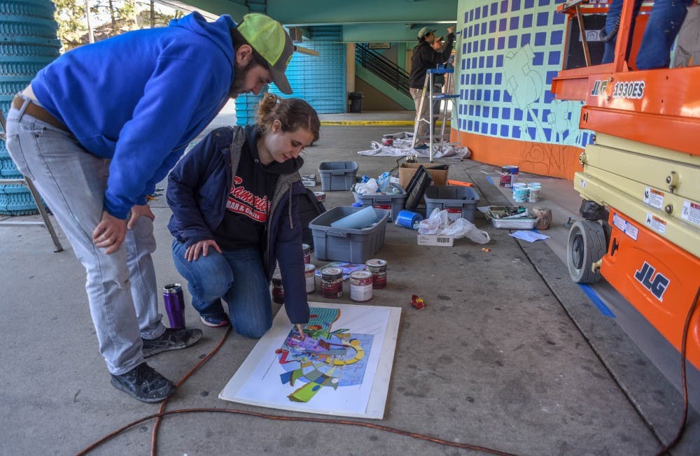 <p>Project members Andrew Somoskey, left, and Emily Somoskey, right, plan what to paint on the mural on the corner of Division Street and Albert Avenue on May 14, 2019. A mix of faculty, undergrad and graduate students from the MSU Art Department are working on the project titled “The Groovy Opportunity”. This installment is the first of a five year plan. Each part will be added on to the week of the East Lansing Art Festival. The project involves Ben Duke, Trent Call, Hector Acuna, Emily Somoskey, Andrew Somoskey, Peter Schutt, Kiel Darling and Meghan McCall.</p>