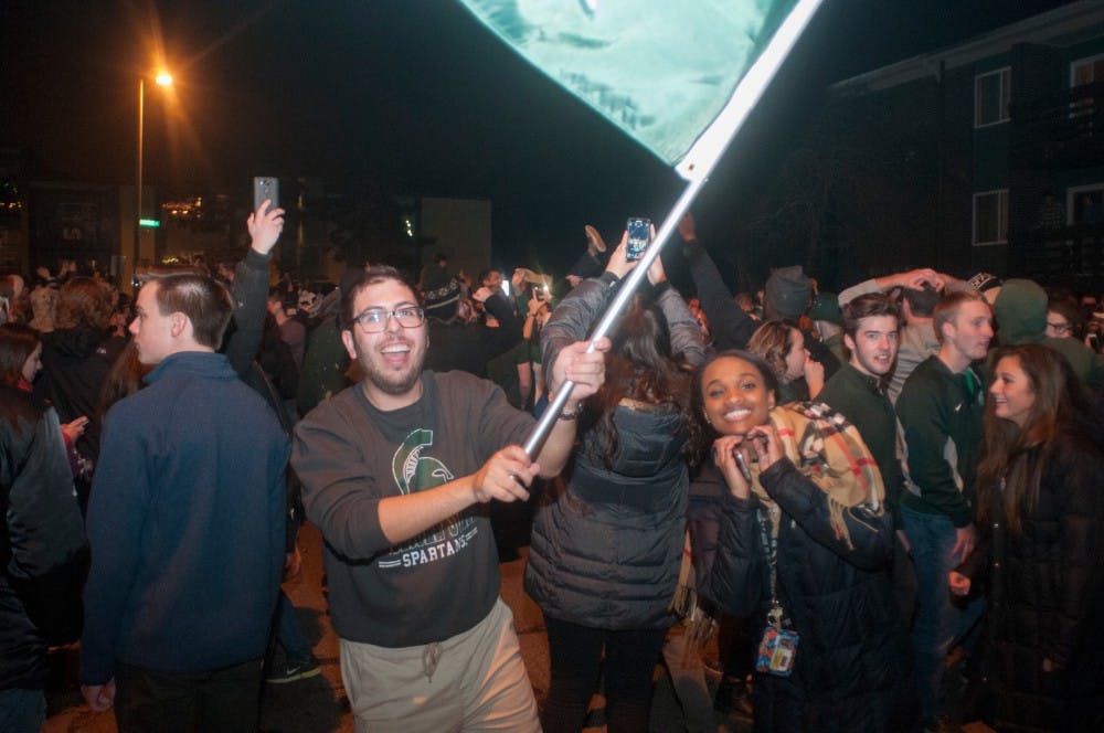 Students wave a MSU flag to celebrate after MSU's victory over Iowa on Dec. 5th, 2015, at Cedar Street.