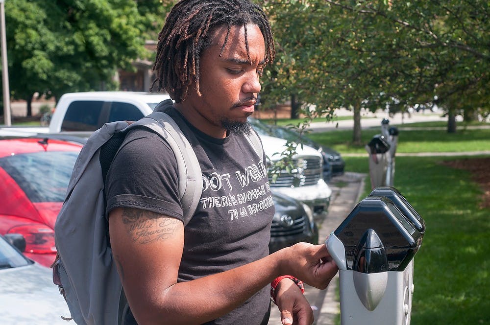 <p>Food industry management senior Brian Dorsey adds money to a parking meter Sept. 9, 2014, at the Olin Health Center parking lot. Raymond Williams/The State News</p>