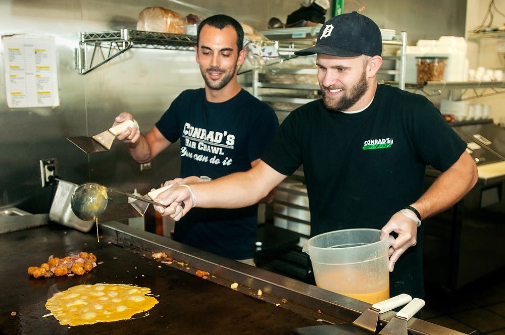 	<p>Lansing resident and manager of Conrad&#8217;s College Town Grill Brian McIsaac, left, cooks and jokes with East Lansing resident and recent <span class="caps">MSU</span> alumnus Pat Rademacher, right, July 16, 2013, at Conrad&#8217;s College Town Grill, 101 E. Grand River Ave. Joe Conrad, the owner, was originally the owner of both Conrad&#8217;s and Menna&#8217;s Joint. Danyelle Morrow/The State News</p>