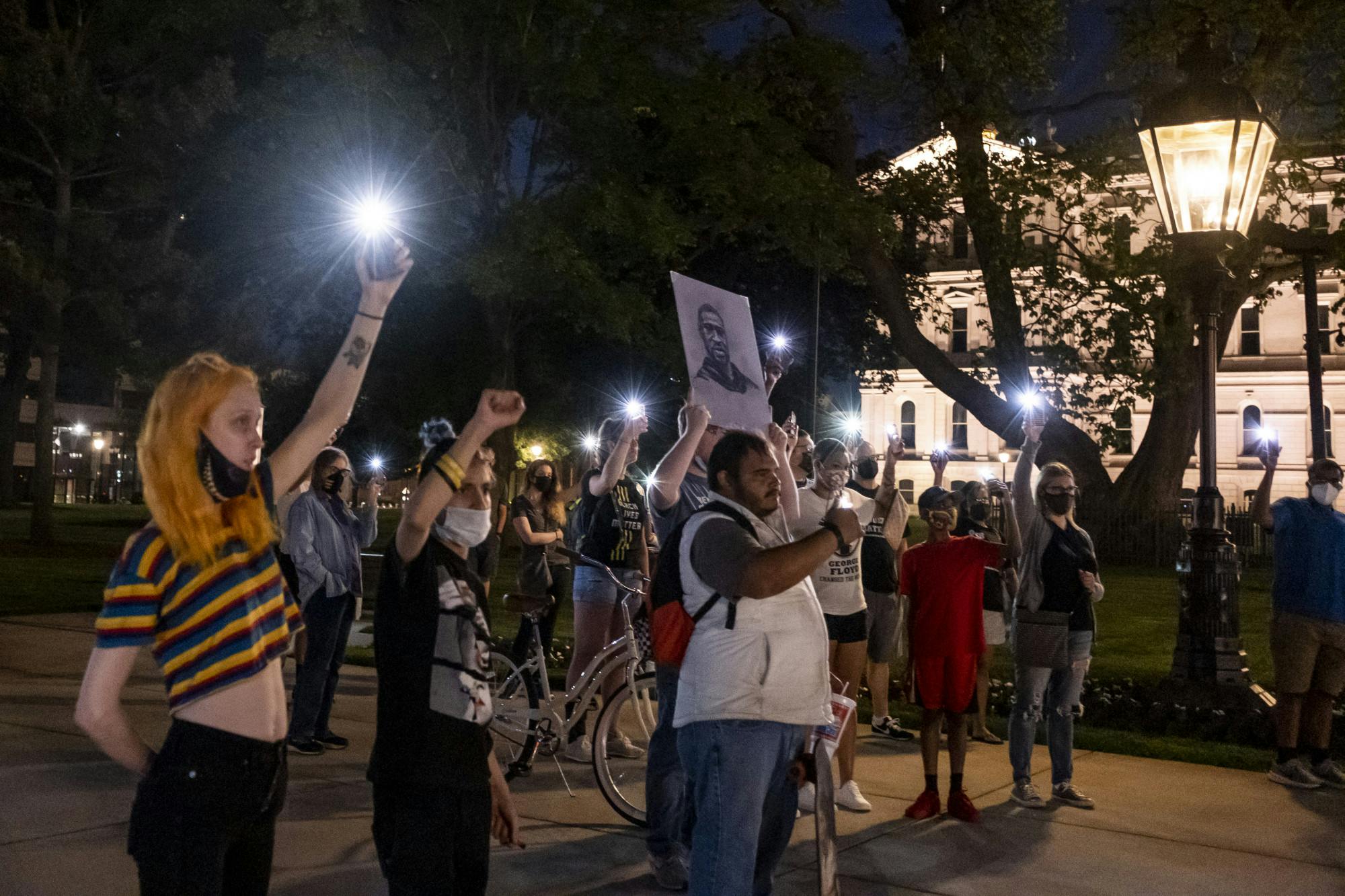 <p>Gatherers at the event for the one-year anniversary of George Floyd&#x27;s death hold up their phone flashlights and a portrait of George Floyd at Michigan&#x27;s Capitol building on May 25, 2021.</p>