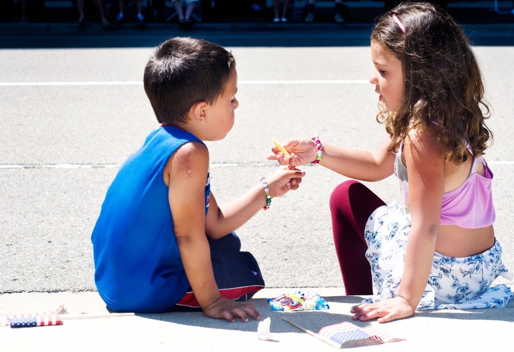 	<p>East Lansing resident Sommer Aljaari, 5, offers her brother Juston, 4, a piece of candy she picked up at the City of Lansing July 4th parade marches past them Monday afternoon on W. Allegan St. A parade of clowns, community groups, and specialty automobiles made their way around the Michigan State Capitol Monday morning to celebrate America&#8217;s independence.</p>