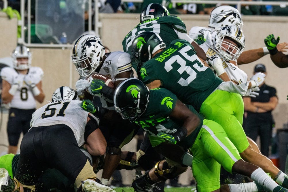 <p>Senior Linebacker Joe Bachie Jr. (35) and junior linebacker Antjuan Simmons (center) tackle a Western Michigan player. The Spartans defeated the Broncos, 51-17, at Spartan Stadium on September 7, 2019. </p>