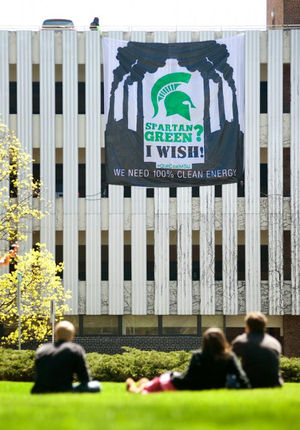From left, psychology junior Mike Tiura, history, shilosophy, and sociology of science sophomore Jordan Lindsay, and hospitality business freshman Adam Woznicki sit by the lawn outside Kedzie Hall on Monday afternoon as they watch members of the MSU Greenpeace hold a banner from the top of Ramp 2 on Auditorium Road. Justin Wan/The State News