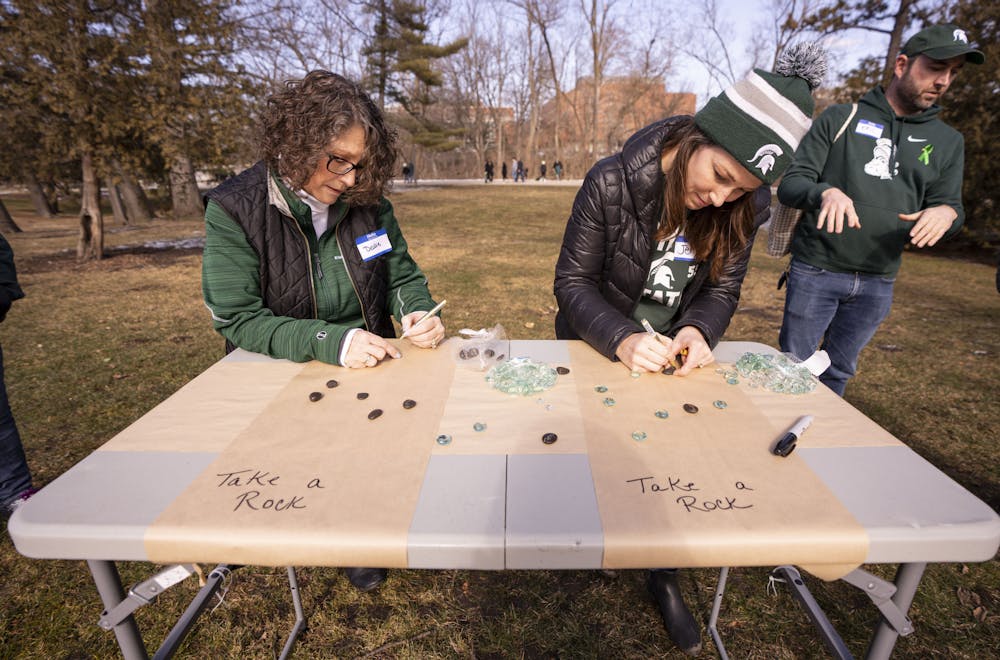 <p>Debbie Stevenson (left) and Jenni Dickins (right) paint messages on rocks on Sunday, Feb. 19, 2023, for Spartan Sunday - an event organized by alumni and Spartan parents to welcome students and faculty back to campus. “We wanted to bring good sentiments people could take with them and, whenever they’re ready, they can hold their little rock and remember that people care about them,” Dickins said.</p>