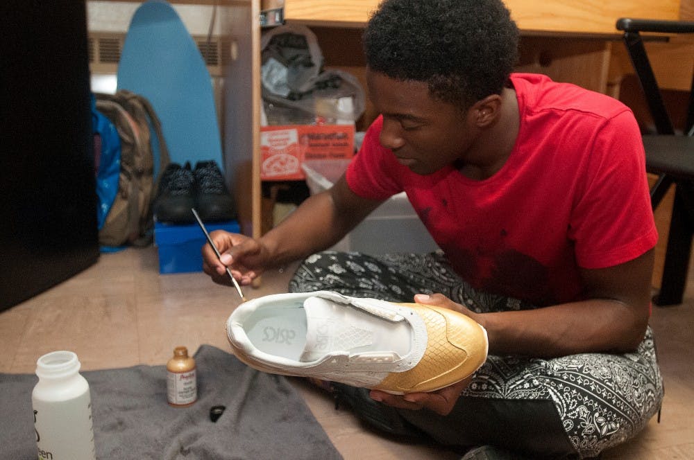 <p>Chemistry freshman Jonathan Brown adds his own touch to ordinary sneakers Sept. 10, 2015, in his Hubbard dorm room. Jonathan hopes to someday open his own shoe boutique. Kennedy Thatch/The State News</p>