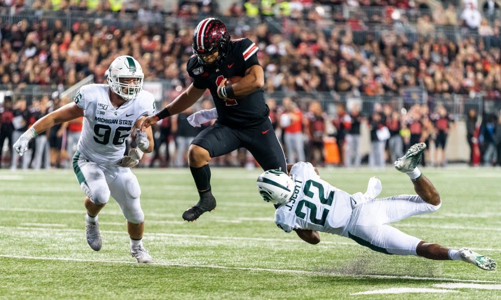 <p>Then-Ohio State quarterback Justin Fields (center) tries to hurdle then-junior cornerback Josiah Scott (22). The Buckeyes defeated the Spartans, 34-10, at Ohio Stadium on Oct. 5, 2019. </p>