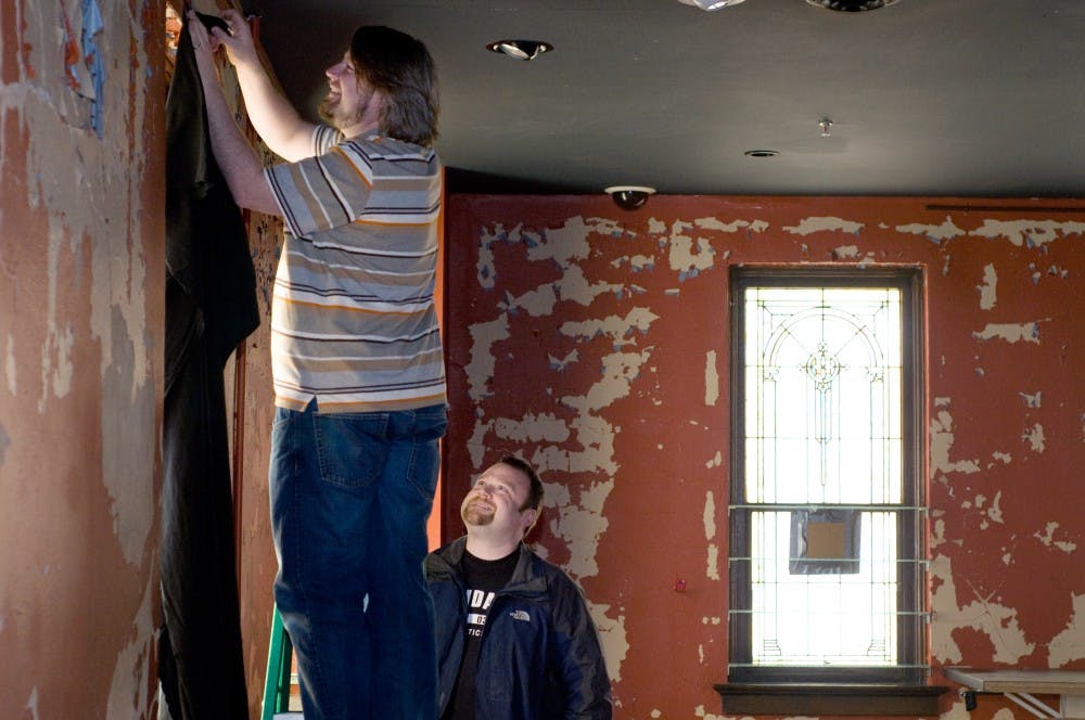Lansing residents Jason Gabriel, above, and Dominic Cochran hang fabric to cover the windows of Temple Club, 500 E. Grand River, Lansing, on Wednesday to prepare for the Capitol City Film Festival that will be held there today through Sunday. Gabriel and Cochran are two of three cofounders of the festival and were preparing the building for this weekend's event. Kat Petersen/The State News