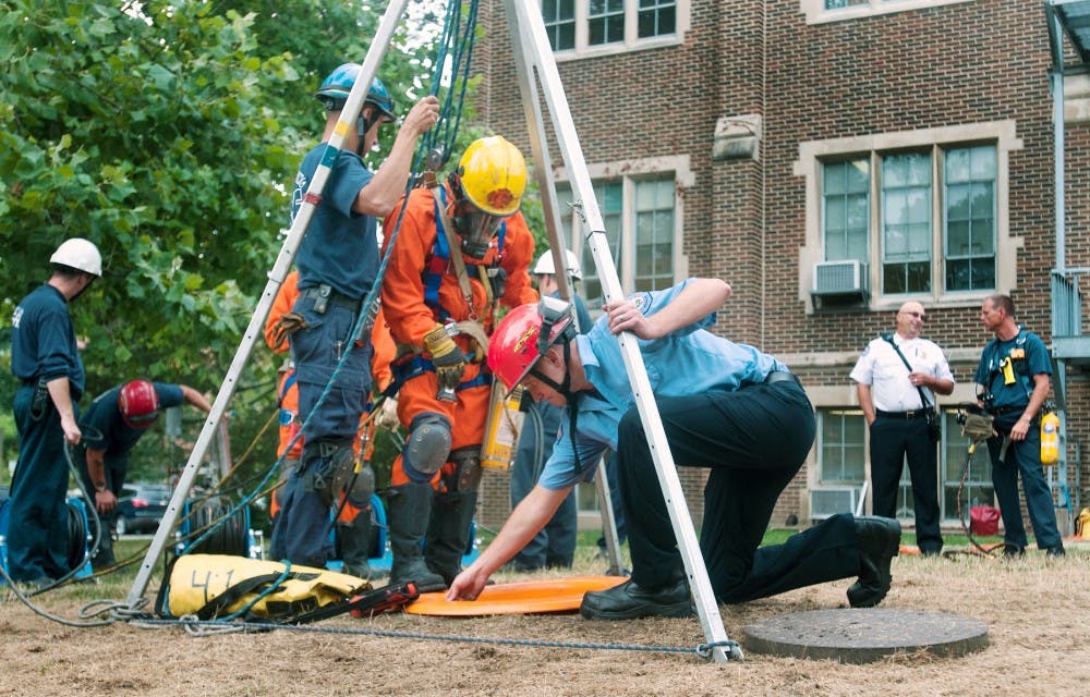 Lansing firefighter Chad Sims, center, prepares to enter a manhole during a confined space rescue training outside the MSU Museum on Aug. 8, 2012. Firefighters who went down the manhole had to do so with their arms placed upward because of the lack of space. Julia Nagy/The State News