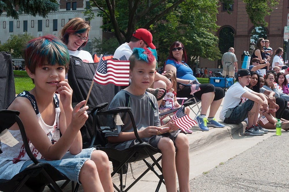 <p>As motorcycles and antique cars rumbled down the street, Lillian Yunker, 9, and Zachary Yunker, 7, waved their flags during the parade July 4, 2015 in Lansing. They got into the spirit of Independence Day this year by dyeing their hair red and blue, along with their mother, Lauren Yunker (behind). Catherine Ferland/ The State News</p>