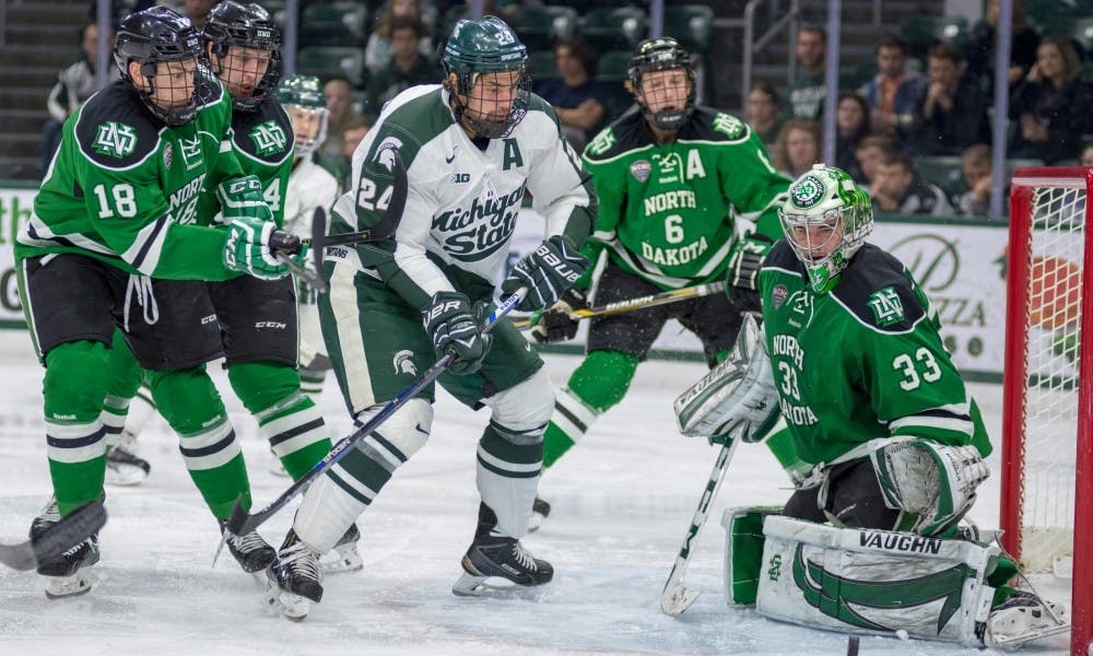 Senior forward Justin Hoomaian shoots the puck as he is defended by North Dakota forward Chris Wilkie, 18, and North Dakota goalie Cam Johnson, 33, during the first period of the game against North Dakota on Nov. 29, 2015 at Munn Ice Arena. The Spartans lost against the Fighting Hawks, 4-1.