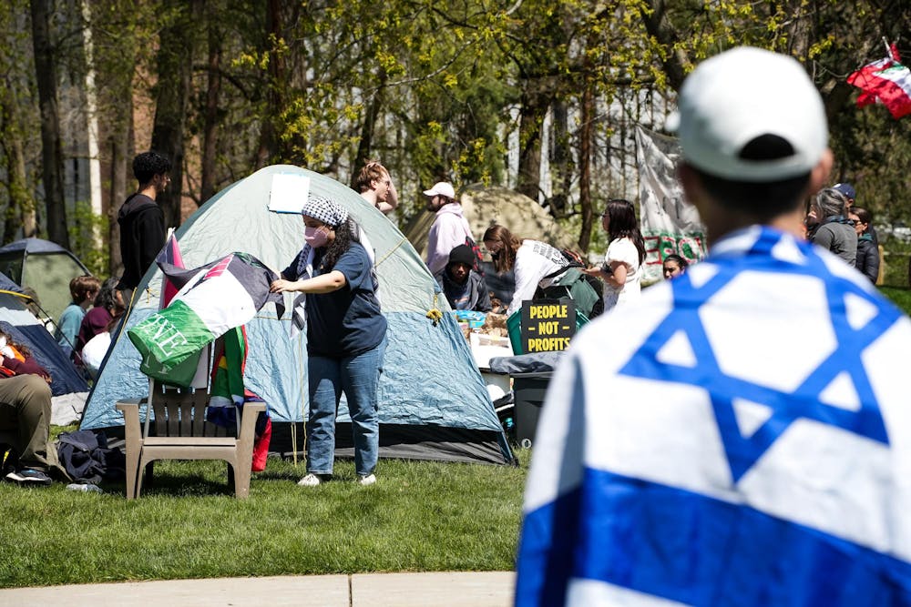 A Michigan State University student draped in the flag of Israel looks onto the Gaza solidarity encampment in People’s Park on MSU’s campus on April 25, 2024.