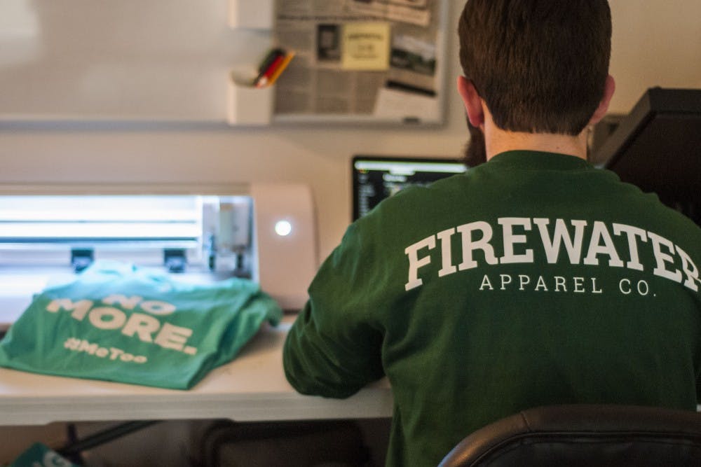 East Lansing resident and MSU alumnus Austin Pabian sits at his desk where he designs his shirts for his company, Firewater Apparel, on April 10, 2018. (C.J. Weiss | The State News)