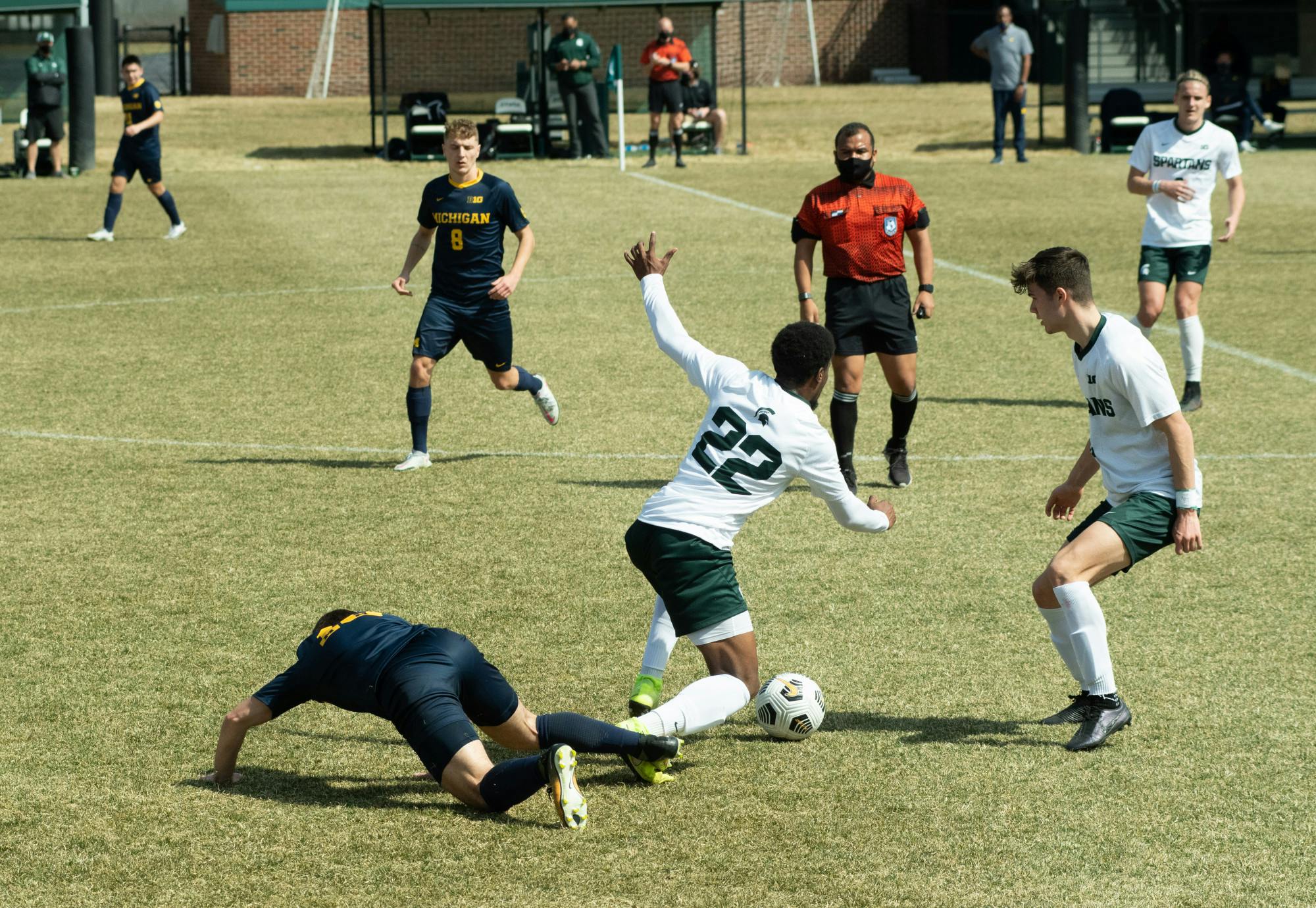 A fallen University of Michigan player trips Michigan State's Will Perkins (22) during the Spartans' loss on March 23, 2021.