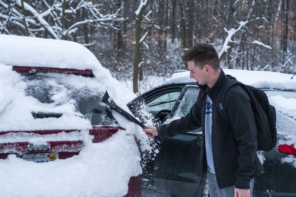 <p>Junior advertising management major Dom Rea brushes the snow off his car to prepare to drive to IM Sports East to play some basketball on Feb. 8, 2018 at Waters Edge apartments. (C.J. Weiss | The State News)</p>