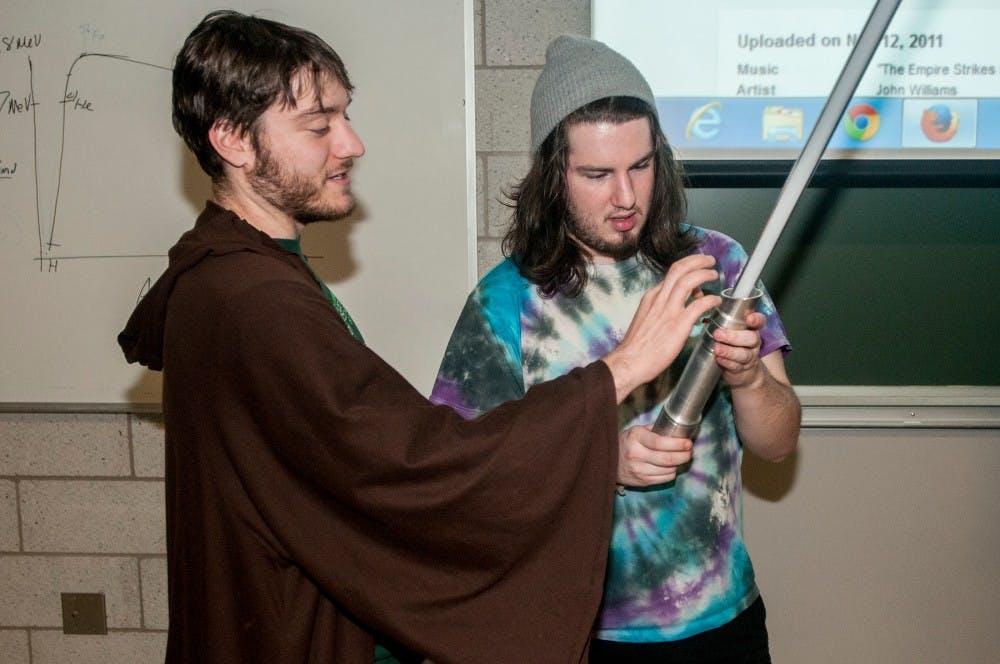<p>From left, food industry management senior Erik Dudek shows advertising junior Grant Barnes his handmade lightsaber Nov. 20, 2014, at the Biomedical and Physical Sciences Building. Dudek is the president of the MSU Jedi Council, an MSU Star Wars fan club. Raymond Williams/The State News</p>