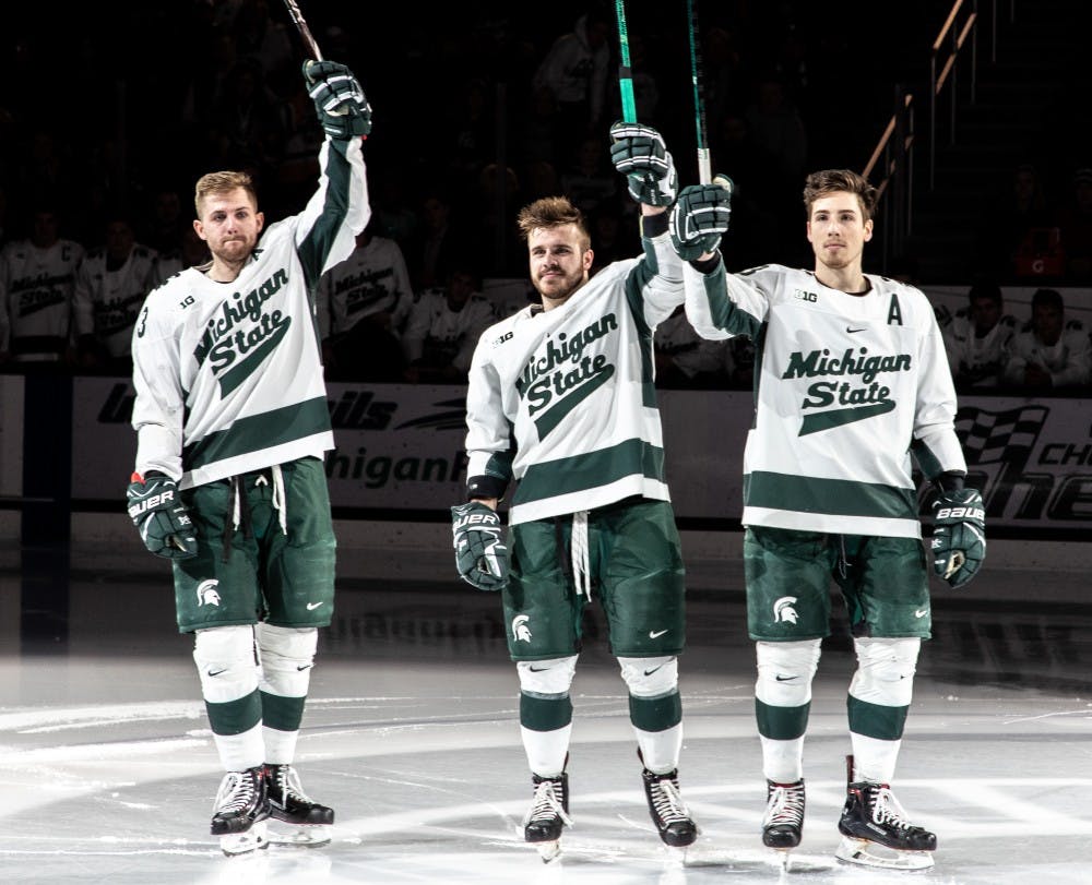 <p>Seniors Cody Milan (23), Zach Osburn (2), and Brennan Sanford (13) raise their sticks to the crowd prior to the game against Penn State Feb.16, 2019. The Spartans trailed the Nittany Lions 2-1 after the first period.</p>