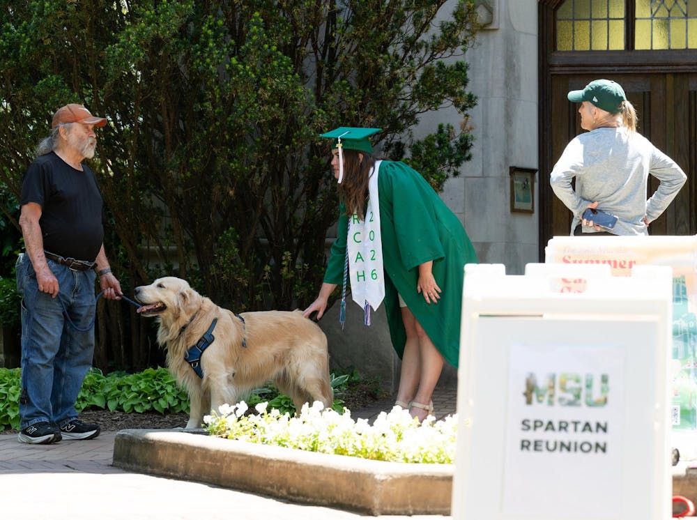 <p>A recent MSU grad talks with frequent campus visitor Raymond the golden retriever and his owner Mike Harju by Beaumont Tower in East Lansing, Mich., on May 28, 2026.</p>