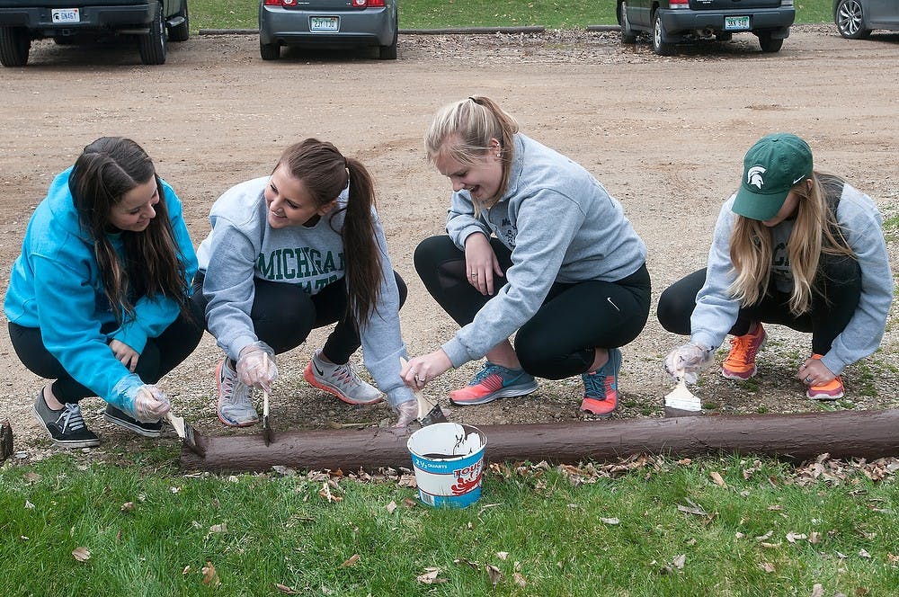 <p>(From left to right) Human resource management sophomore Nicole Kunecki, nutritional sciences junior Jade Woodruff, elementary education sophomore Beth Henley, and physiology junior Amber Johnson paint a log April 25, 2015, at Lake Lansing Park South, 1621 Pike St. in Haslett. All four girls are members of Sigma Kappa sorority and were cleaning up the park by painting, picking up garbage, and shoveling wood chips along with other members of the Greek community. Allyson Telgenhof/The State News.</p>
