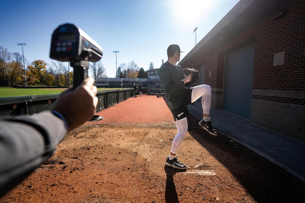 Michigan State redshirt junior right-handed pitcher Ryan Szczepaniak (42) pitches in the bullpen during pitching practice at McLane Stadium on Nov. 7, 2024. MSU Baseball assistant and pitching coach Mark Van Ameyde tracks the speed of the pitch using a radar gun.