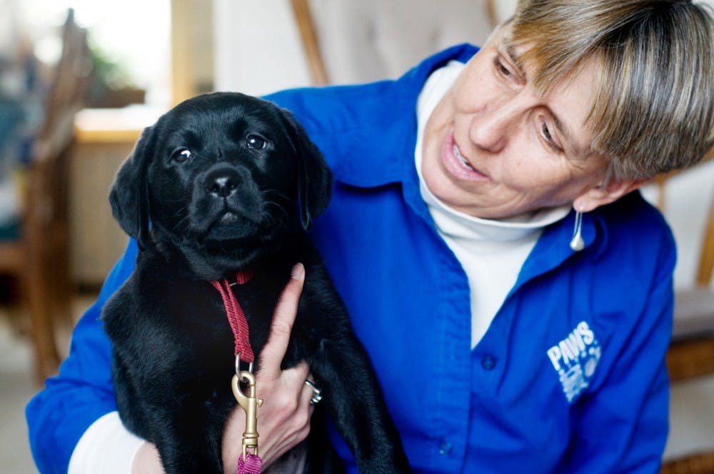 Puppy raiser Carol McEllhiney-Luster holds her new black lab puppy, Bess, Friday at her home in East Lansing. McEllhiney-Luster has been raising puppies for four years through Paws with a Cause, a national program that raises assistance dogs for people with disabilities. Matt Radick/The State News