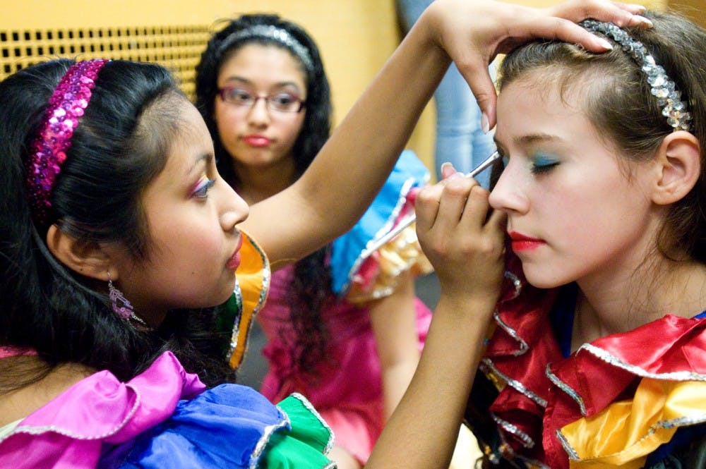 Lansing resident Lena Garcia, 16, left, puts eyeshadow on Lansing resident Emily Sanchez-Weiss, 12, while Lansing resident Thalia Esparza, 14, watches before the girls go on stage to dance for the crowd that gathered at the annual Dia de la Mujer conference Saturday at Kellogg Center. The event is held to celebrate Chicana and Latina women and their accomplishments. Kat Petersen/The State News 