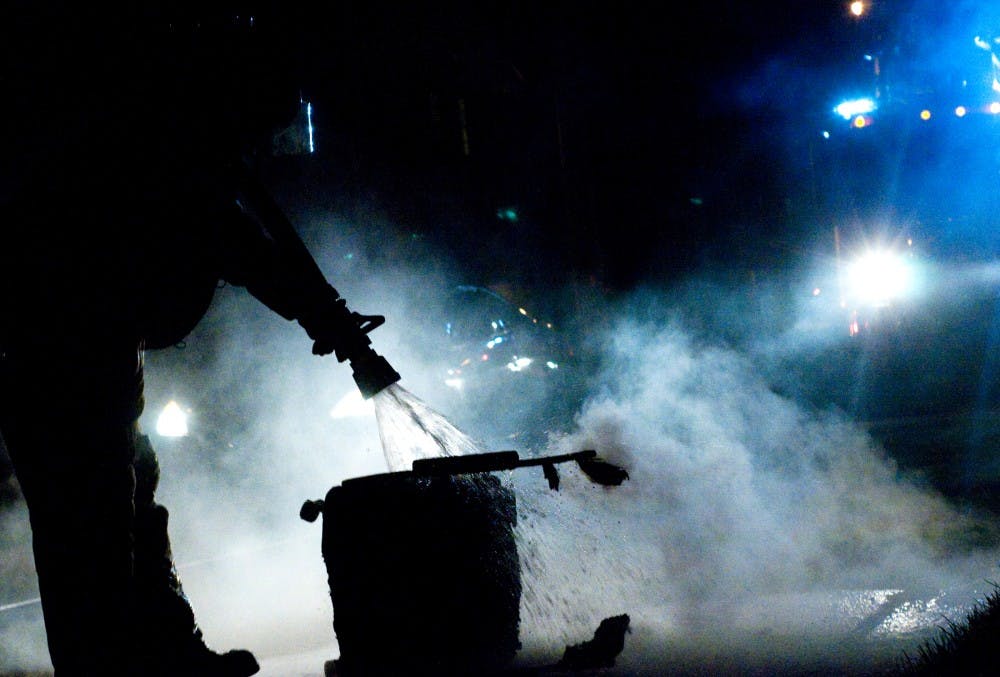 East Lansing fire fighter Chuck Gagnier uses a fire hose to douse a burning chair on Elm Street in East Lansing after Michigan State lost to Louisville in the Sweet Sixteen earlier in the evening. Samantha Radecki/The State News