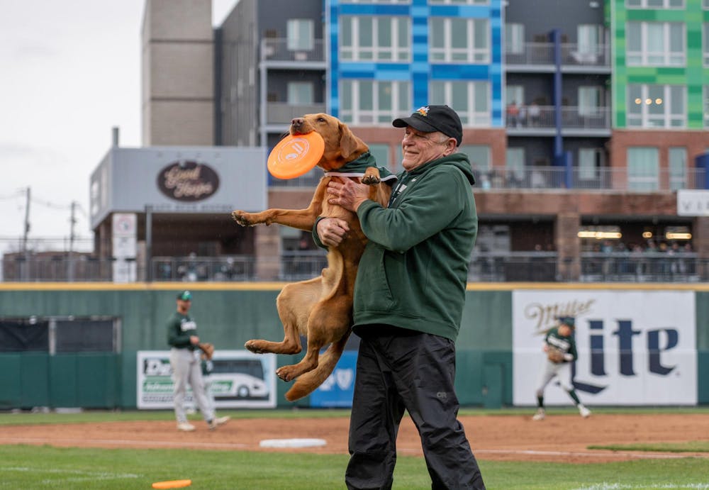 Zeke's handler scoops him up after a round of frisbee-throwing at Jackson Field during the "Crosstown Showdown" in Lansing, MI, on Wednesday, April 3, 2024.