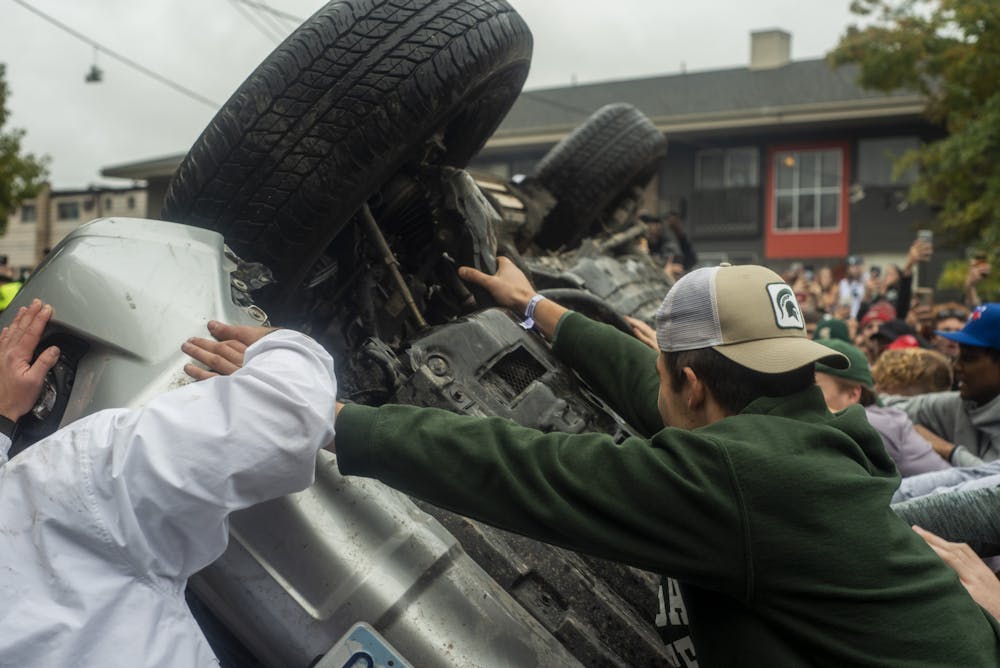 <p>People flipping a car onto its back at the Cedar Village apartments after MSU&#x27;s win against U-M on Oct. 30, 2021.</p>