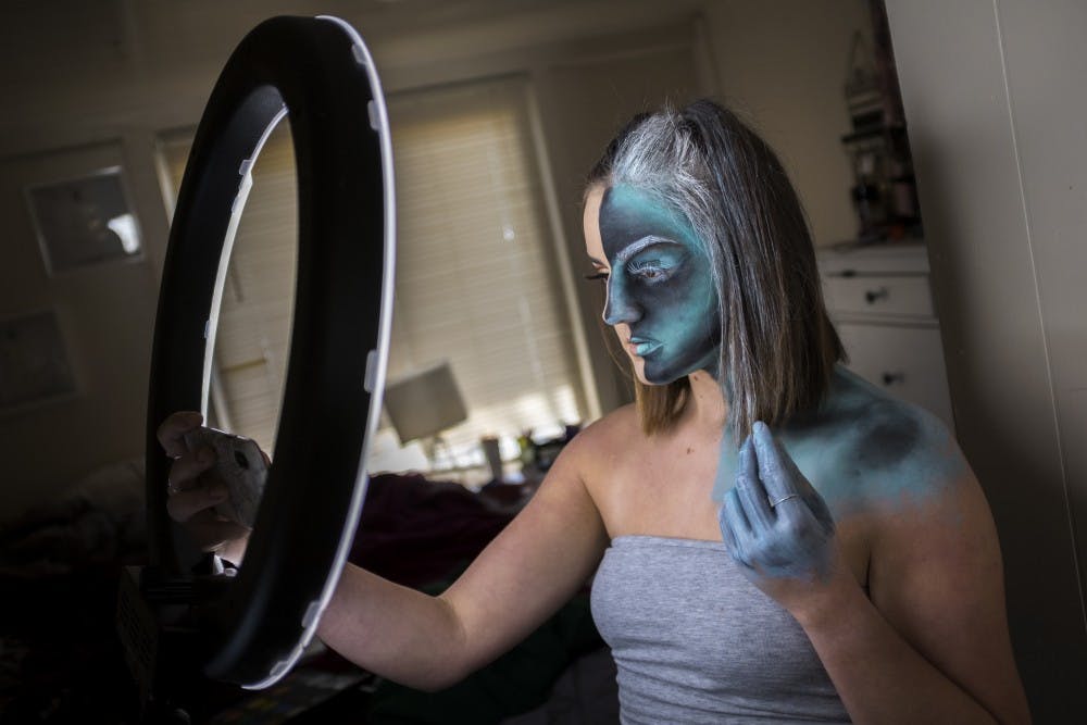 Genetics junior Michaella Andersen uses her phone to take a photo at her home in East Lansing on April 15, 2019. Andersen started drawing elaborate looks on her face a year ago and usually spends 4 to 6 hours on them, with the longest look taking her 7 hours to complete. (Nic Antaya/The State News)