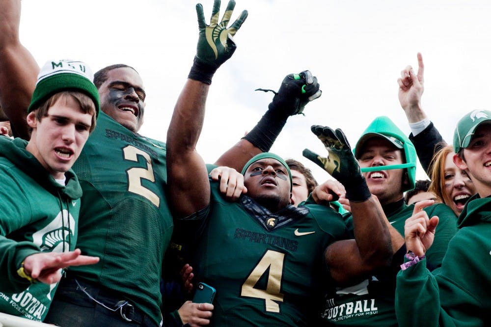 Junior running back Edwin Baker throws up four fingers as he and sophomore defensive end William Gholston join fans in the student section after defeating Michigan 28-14 Saturday afternoon at Spartan Stadium. The win Saturday marks the fourth straight victory the Spartans have had over the Wolverines. Matt Hallowell/The State News