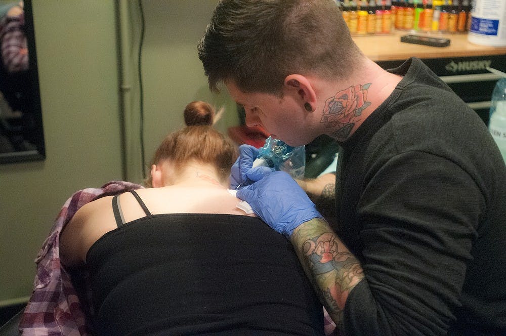 <p>Lansing resident Kim Finnie, left, gets a tattoo done by Corona, Mich., resident Bryce Petoskey on Sept. 12, 2014, at Ink and Needle on Abbott Road. Jessalyn/Tamez The State News </p>
